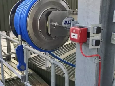 Outdoor medium-pressure stainless steel hose reel with blue hose mounted to a steel structure at an industrial washdown site in Burton.